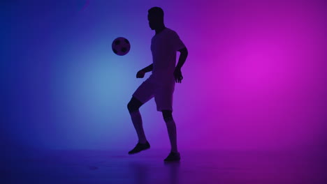 Black-man-a-player-juggles-football-ball-in-a-dark-studio-with-neon-lights-on-the-floor-and-red-and-blue-lighting-effects-in-slow-motion.-African-professional-football-soccer-player